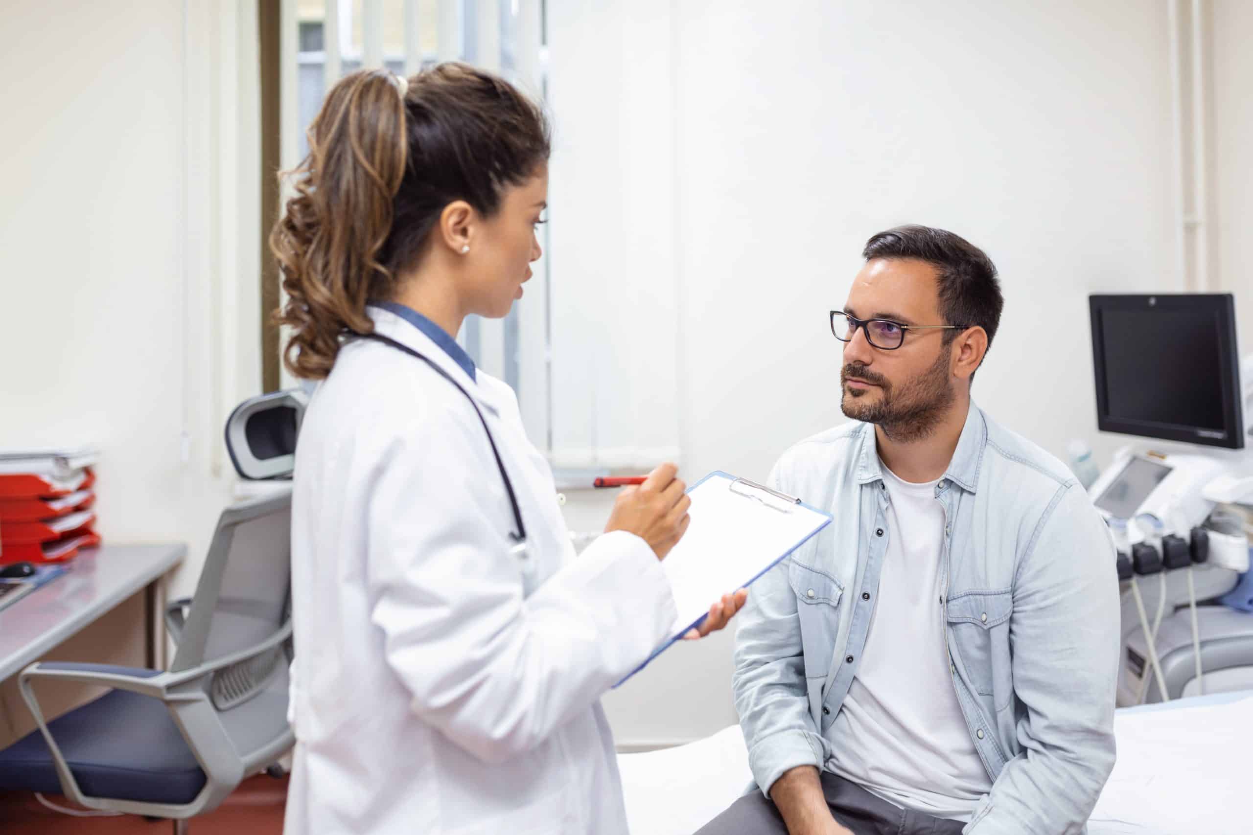 Serious man consulting with young female physician doctor at checkup meeting in hospital. Skilled general practitioner giving healthcare medical advices to patient.